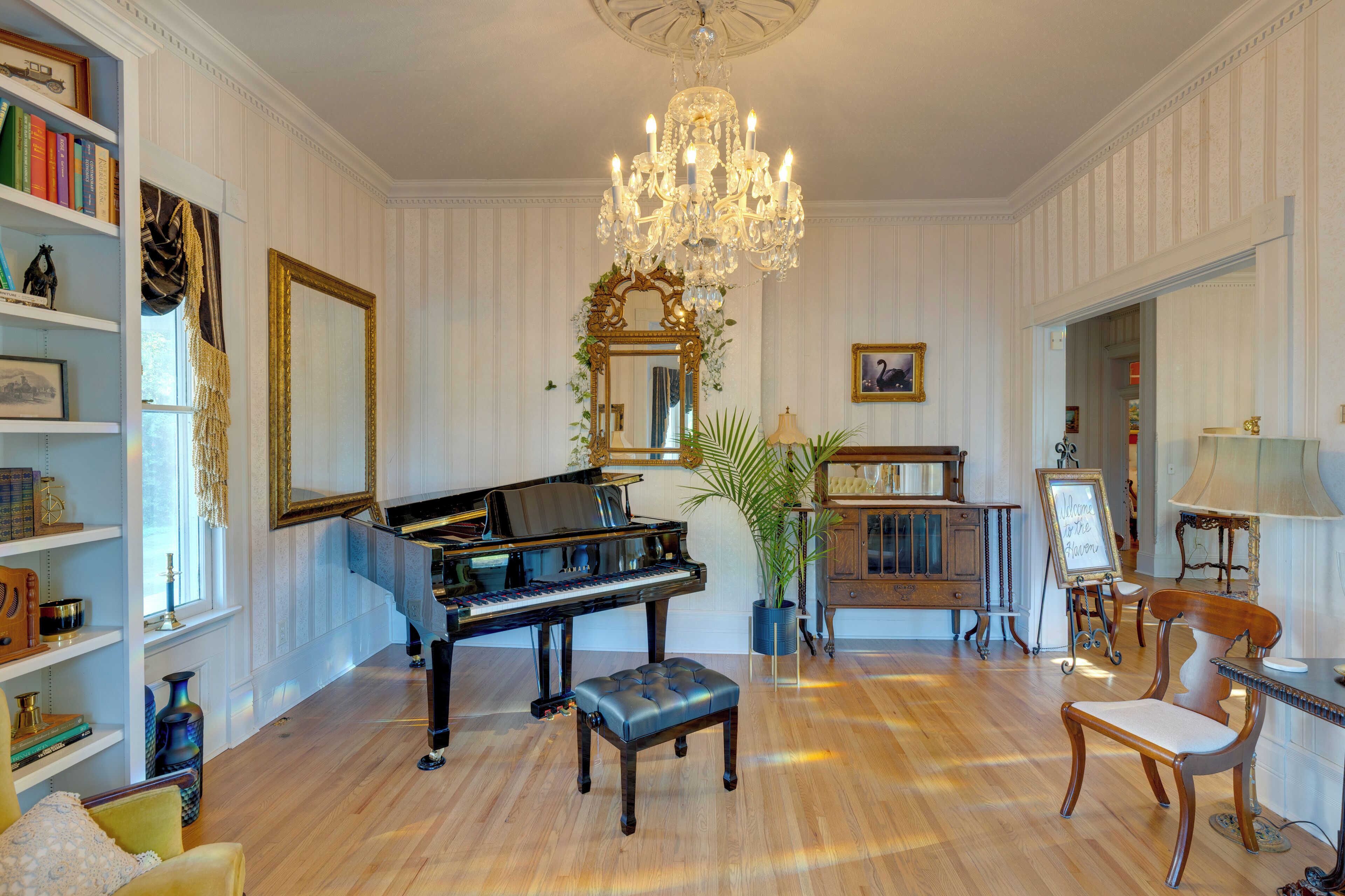 Una sala elegante con un piano, una araña, un espejo y un aparador de madera.
