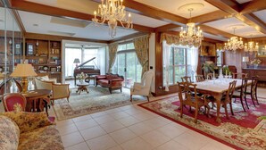 A spacious living room with a grand chandelier, a piano, and a dining area with wooden furniture.
