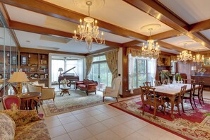 A spacious living room with a grand chandelier, a piano, and a dining area with wooden furniture.