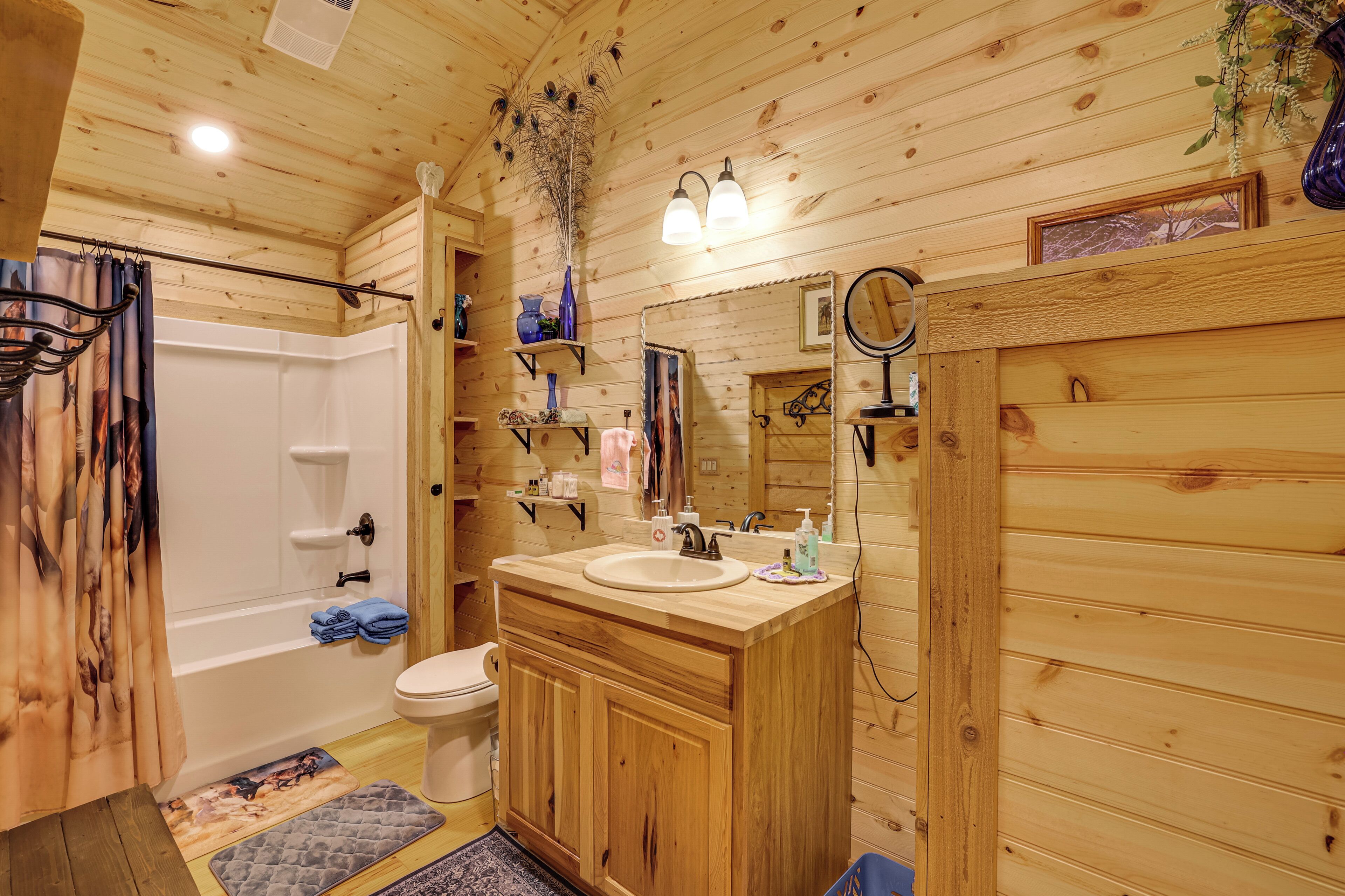 Une salle de bain rustique, aménagée dans une cabane en bois, comprenant une baignoire, des toilettes, un meuble-lavabo avec un évier et un miroir.