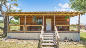 A wooden cabin with a porch, a door, and a staircase leading to a covered area. - Romantic Wine Country Cabin Near Fredericksburg (Harper)