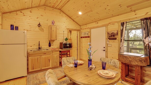 Interior de una cabaña de madera con cocina, comedor y ventana con cortinas.