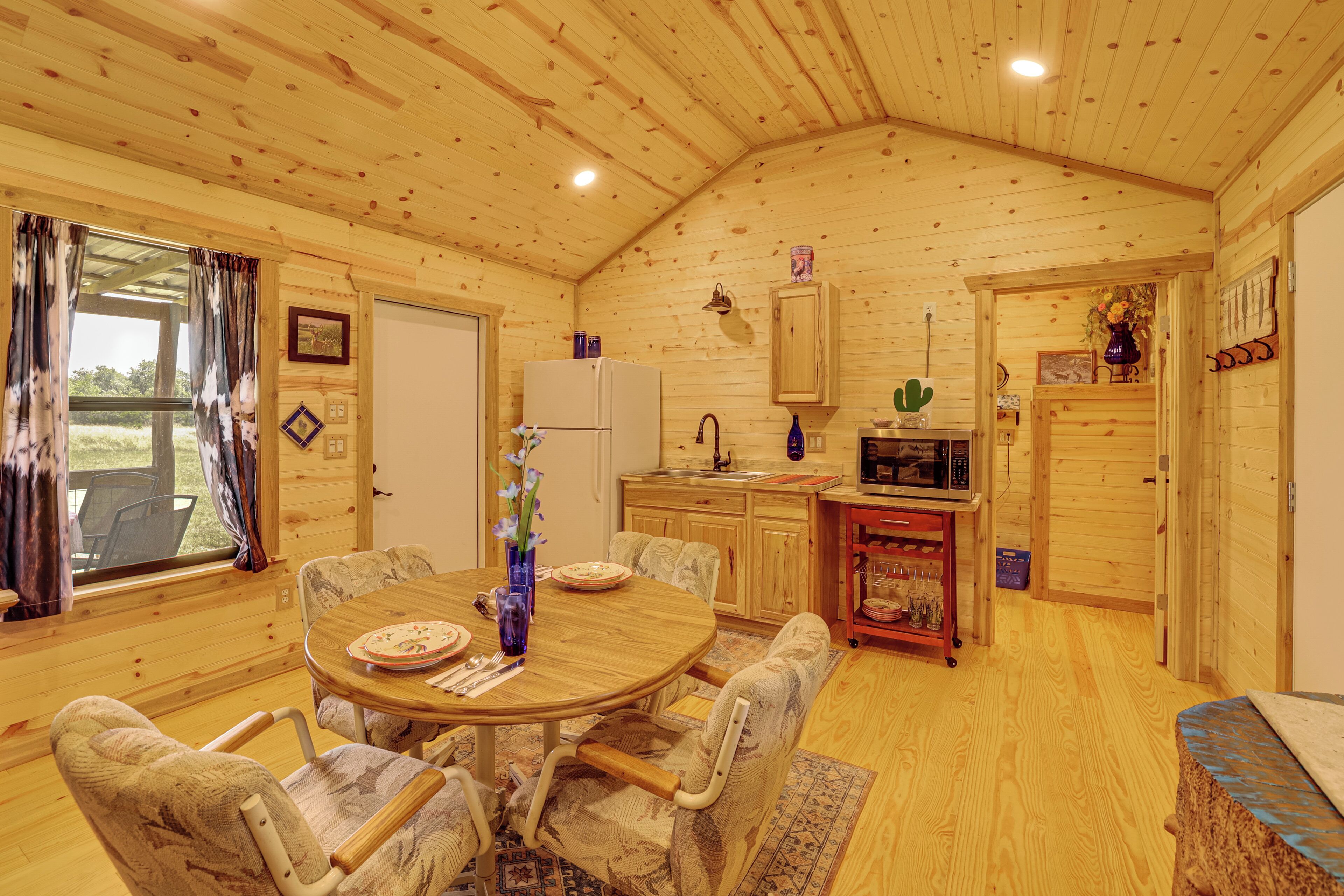Un interior de madera con una mesa de comedor, sillas, un refrigerador, un lavamanos y un microondas.