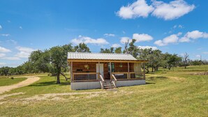 A small wooden cabin with a metal roof, a porch with steps, and a dirt path leading to it. - Romantic Wine Country Cabin Near Fredericksburg (Harper)