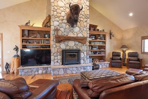 A living room with a stone fireplace, leather sofas, a television, and bookshelves.