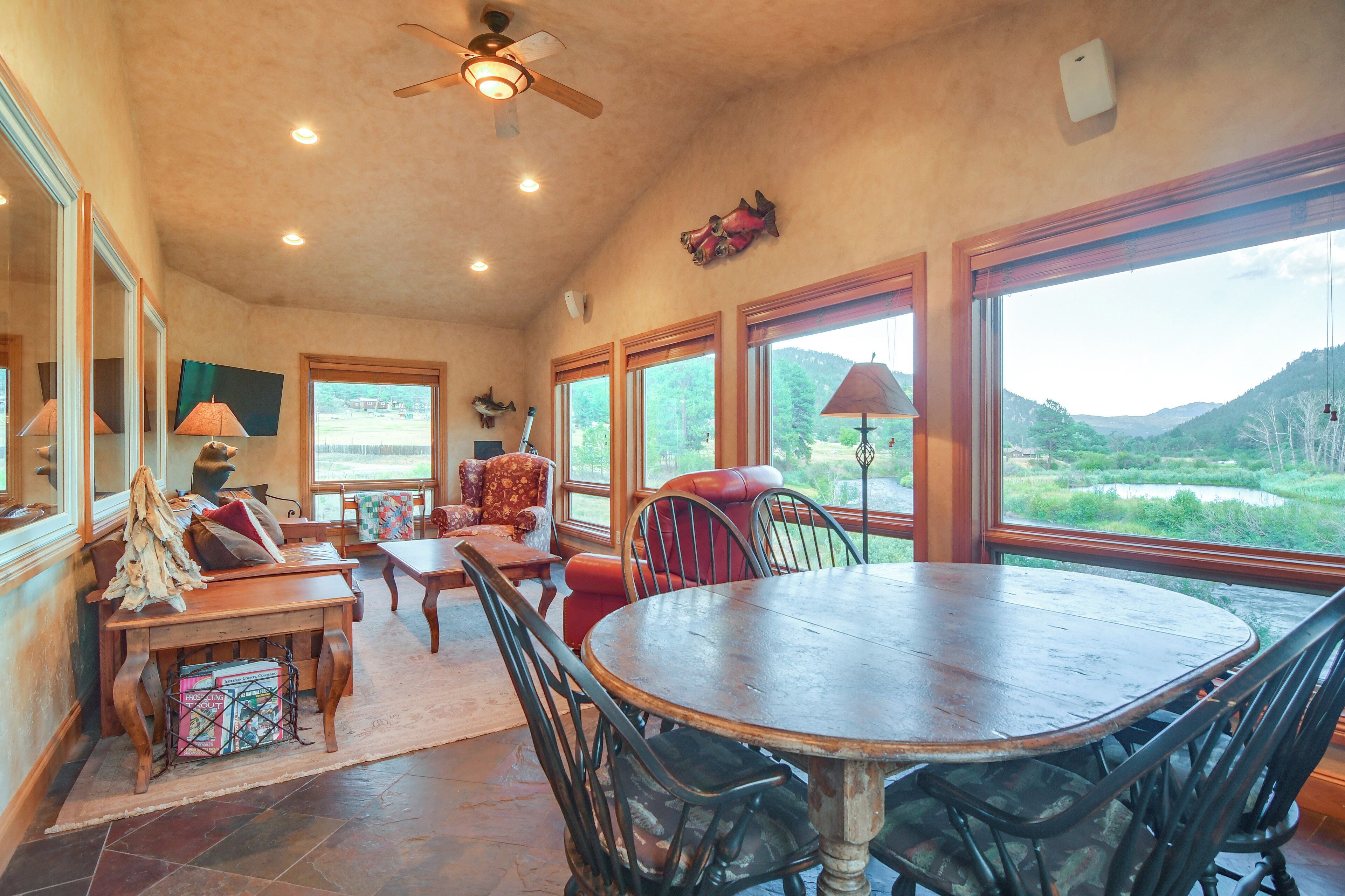A spacious room with a large dining table, comfortable seating, and large windows offering a view of the outdoors.