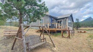 A rustic wooden swing set and a house with a stone foundation and a deck. - Colorado Riverfront Escape! Fish, Hike & Relax (Pine)