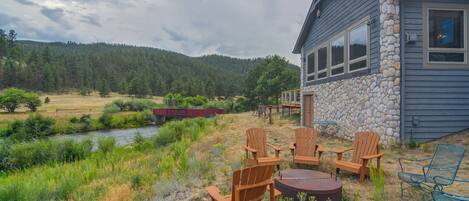 A cabin with a stone exterior, a deck with chairs, and a view of a forested hillside.