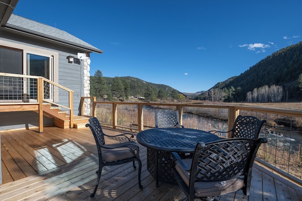 A deck with outdoor furniture, a staircase, and a view of a river and mountains.
