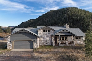 A stone house with a garage, a front porch, and a mountain backdrop.