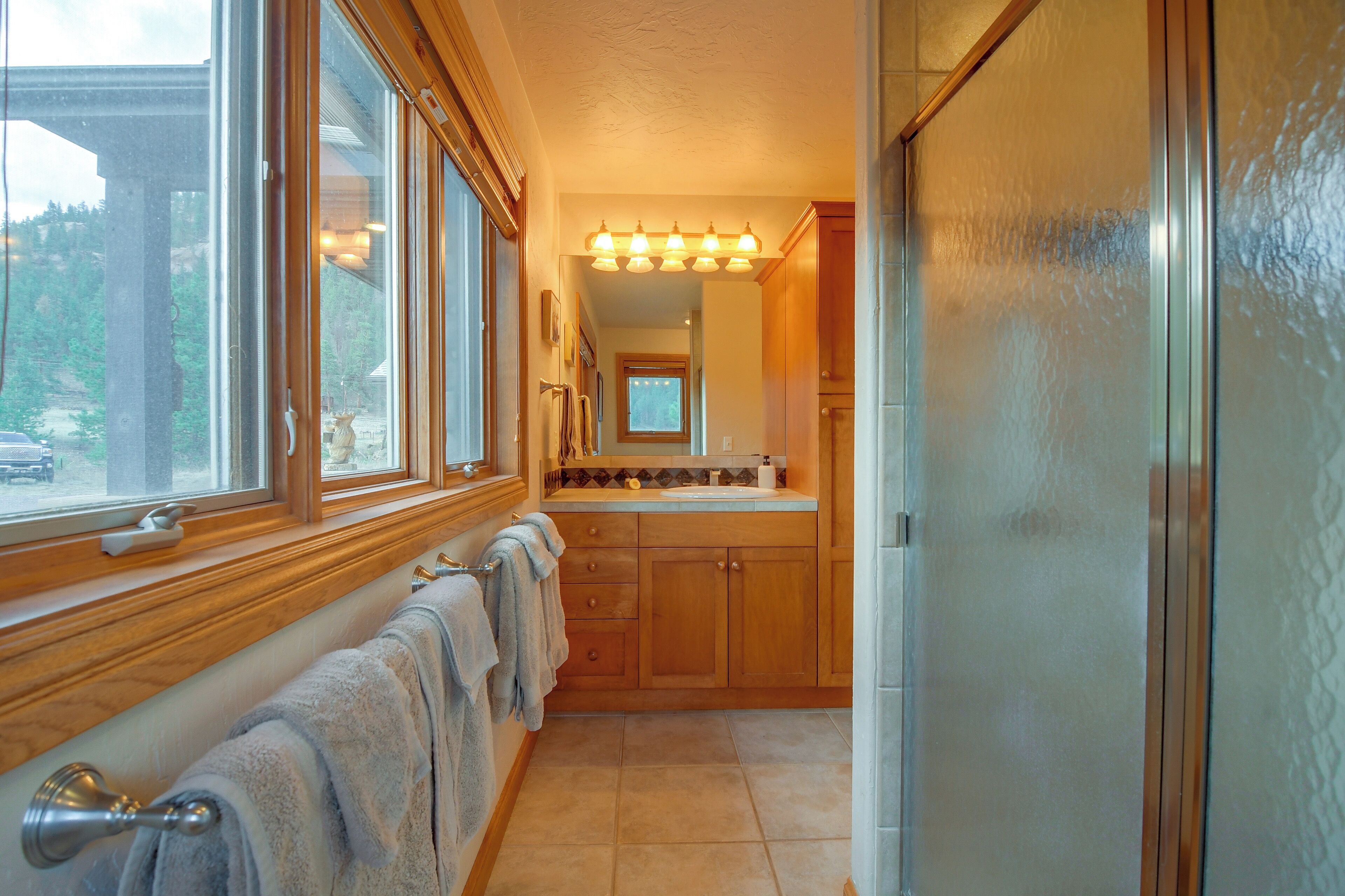 A bathroom with wooden cabinets, a vanity, a mirror, and a window with a view of trees.