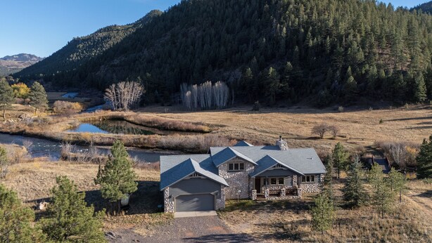 A two-story stone house with a garage, surrounded by a natural landscape with a river and forested hills. - Colorado Riverfront Escape! Fish, Hike & Relax (Pine)