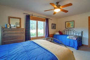 Ein Schlafzimmer mit zwei Betten, einer Kommode, einem Deckenventilator, einem Fenster mit Vorhängen und einem Wandbild.