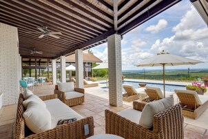 Área externa coberta com móveis de vime, piscina e vista da paisagem.