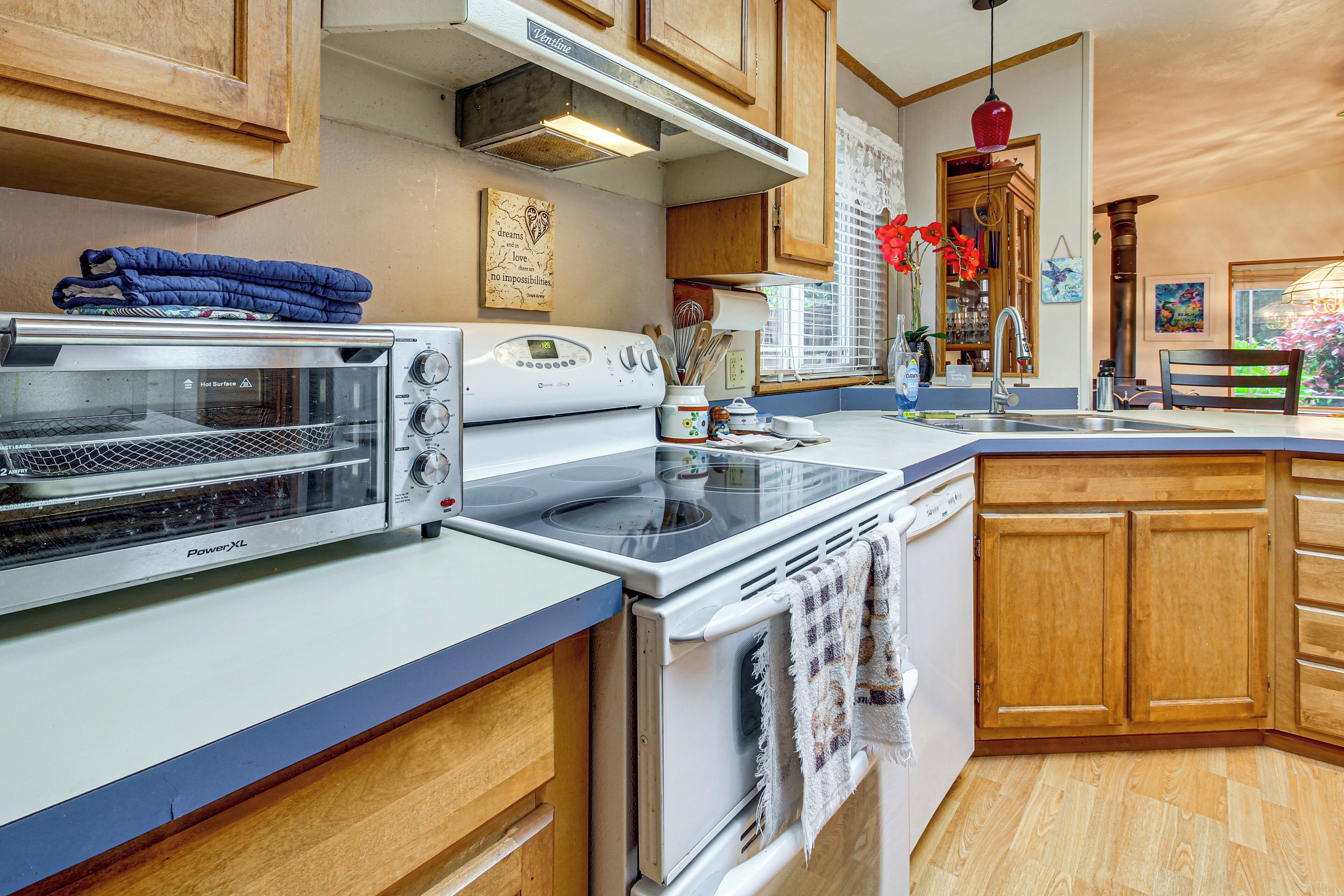A kitchen with a toaster oven, stove, and oven, wooden cabinets, and a window with a view.