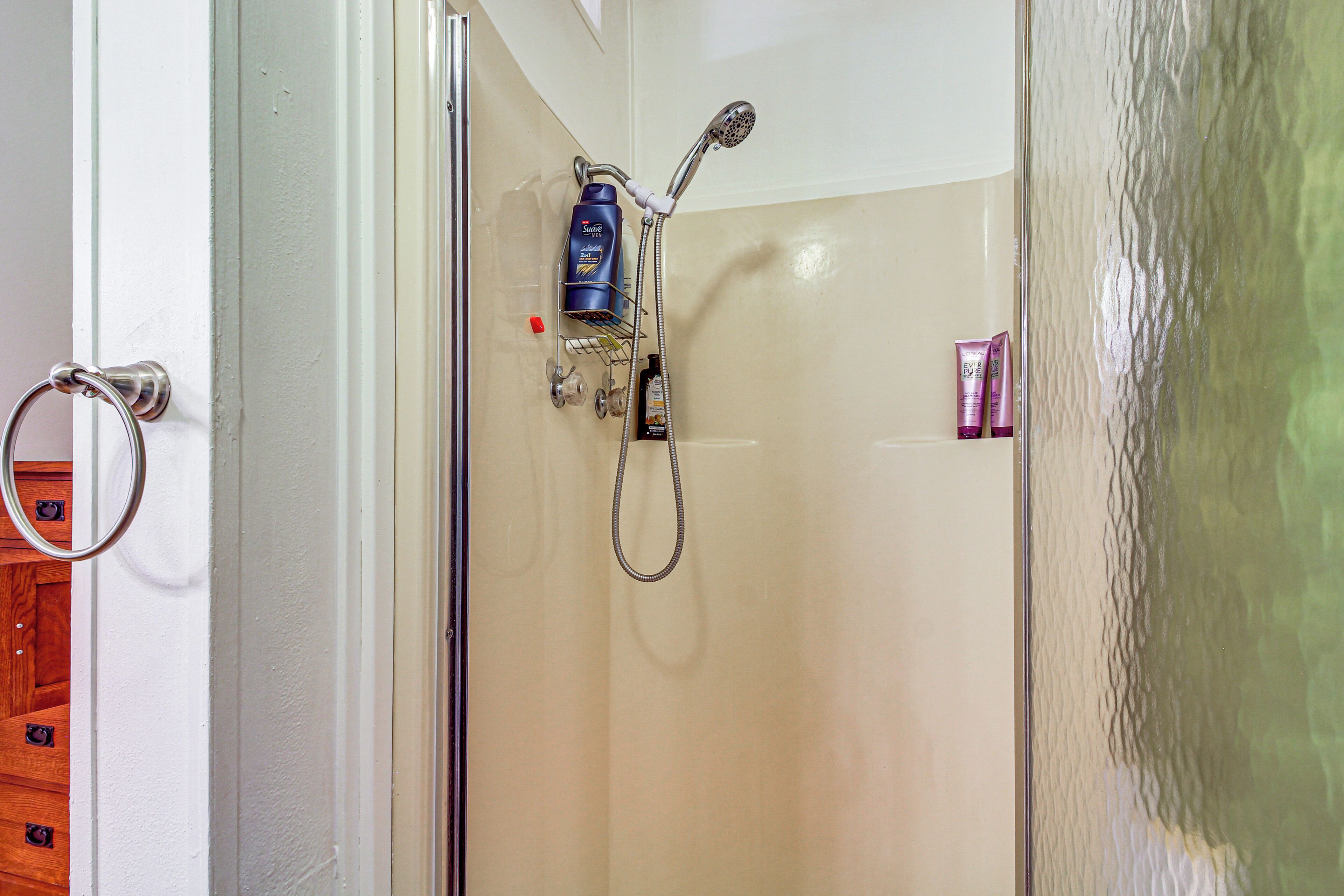 A glass-enclosed shower with a handheld showerhead, a bottle of shampoo, and a soap dispenser.