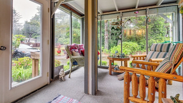 Ein Zimmer mit einer großen Schiebeglaswand, einem Korbstuhl, einer Holzbank mit gestreiften Kissen und einem kleinen Tisch mit Dekoration.