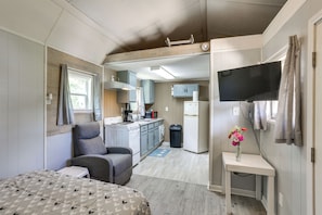 A compact room with a bed, a chair, a small table with a vase, a kitchen area with cabinets and appliances, and a television mounted on the wall. - Peaceful Gulf Coast Getaway: 3 Mi to Boat Ramp! (Orange)