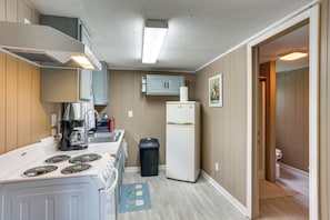 A compact kitchen with a stove, sink, and refrigerator, a trash bin, and a door leading to another room. - Peaceful Gulf Coast Getaway: 3 Mi to Boat Ramp! (Orange)
