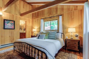 A wooden-paneled bedroom with a bed, bedside tables, a window, and a mirror.