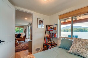 A bedroom with a bed, a bookshelf, a window with a view of a lake, and a door leading to another room. - Private Dock, Deck & Yard: Luxe Sacheen Lake Home (Newport)