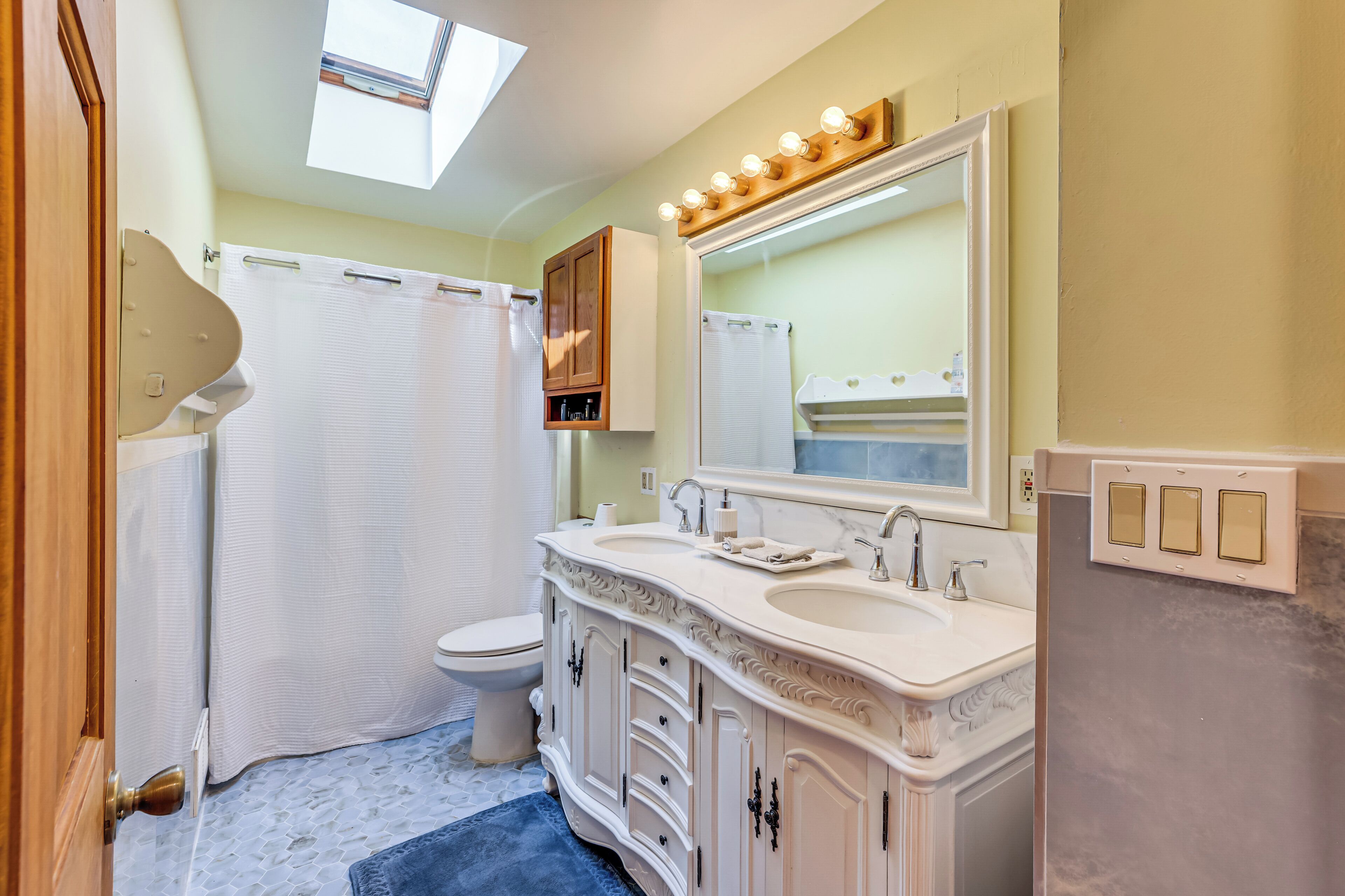 A bathroom with a skylight, a shower curtain, a toilet, a vanity with a mirror, and a sink.