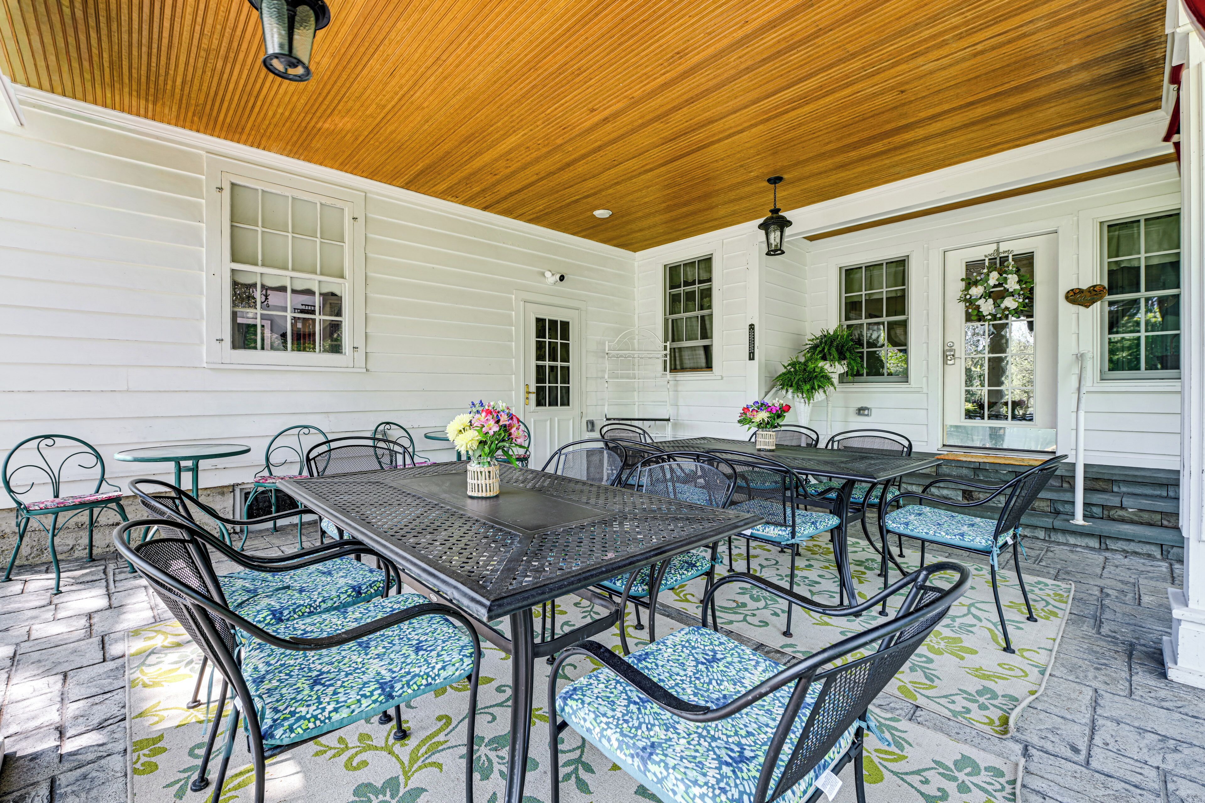 An outdoor patio with a wooden ceiling, white siding walls, and a table with chairs.