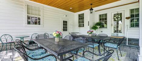 An outdoor patio with a wooden ceiling, white siding walls, and a table with chairs.