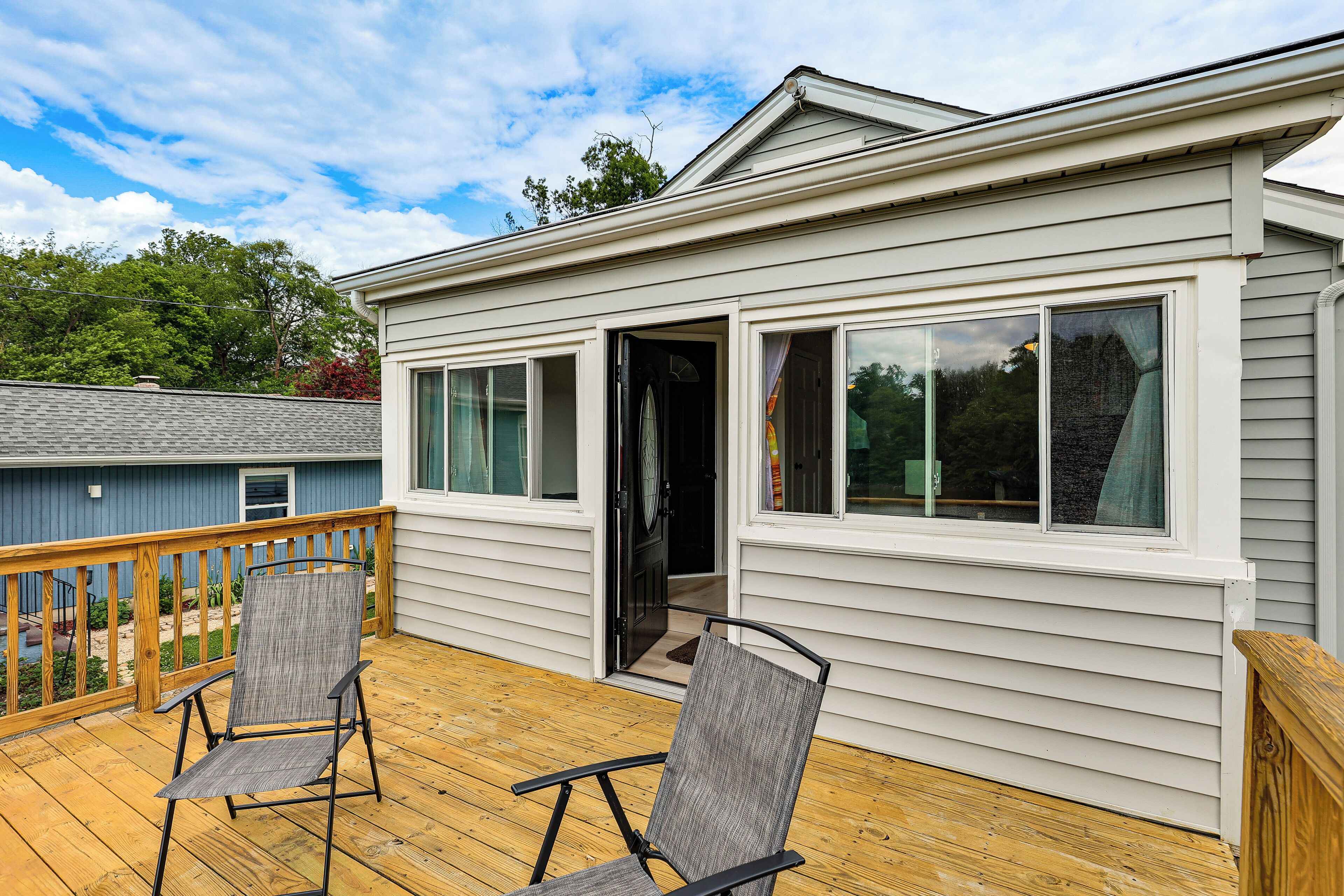 A deck with two chairs, a house with a door open, and a view of the backyard.