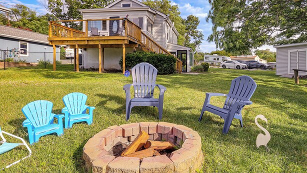 A house with a deck, a fire pit, and blue Adirondack chairs.