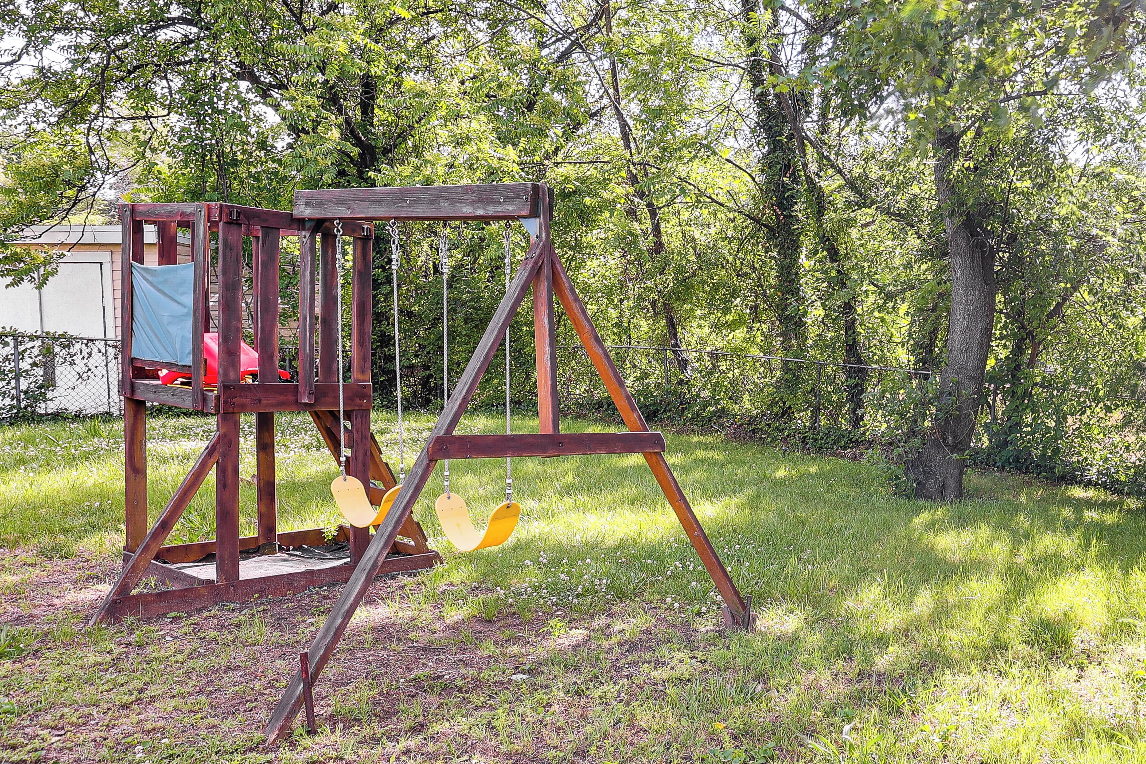 Un ensemble de balançoires en bois installé dans un espace herbeux, avec des arbres en arrière-plan.