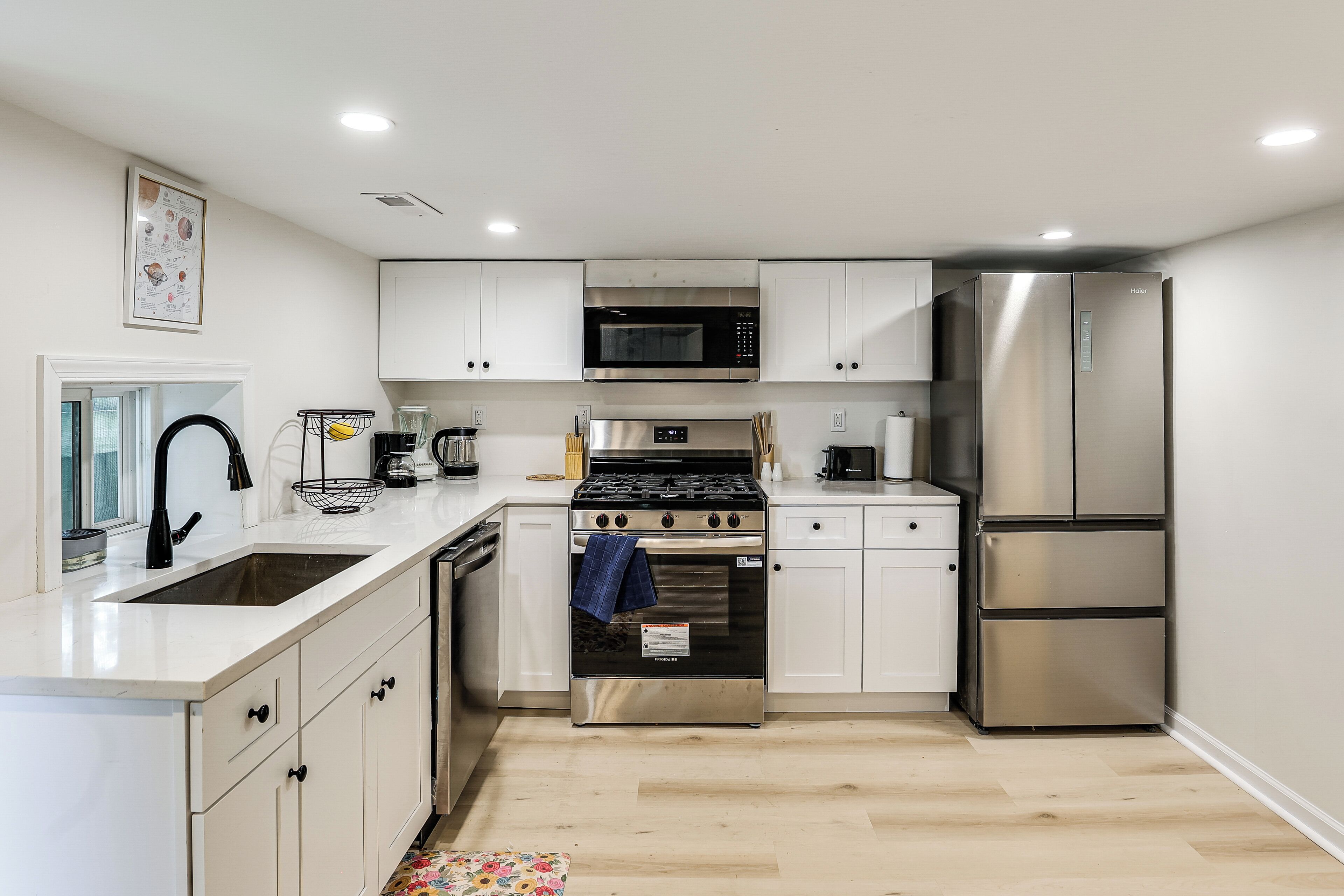 A modern kitchen with white cabinetry, stainless steel appliances, and a wooden floor.