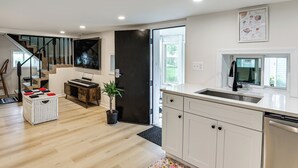 A modern kitchen with white cabinets, a stainless steel dishwasher, and a large window.