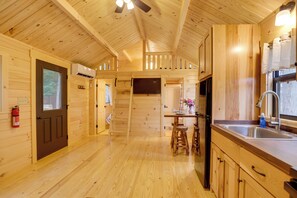A wooden cabin interior with a kitchen area, wooden walls, and a ceiling fan.