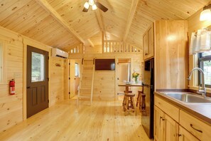 A wooden cabin interior with a kitchen area, wooden floors, and a ceiling fan.