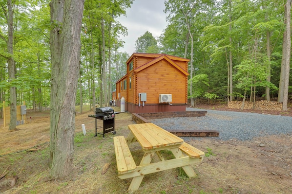 A wooden cabin with a picnic table in a forested area.
