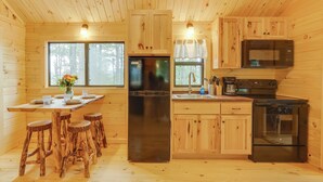 Une cuisine rustique aménagée dans une cabane en bois, avec un îlot central, des appareils en acier inoxydable et une vue sur la forêt grâce à de grandes fenêtres.
