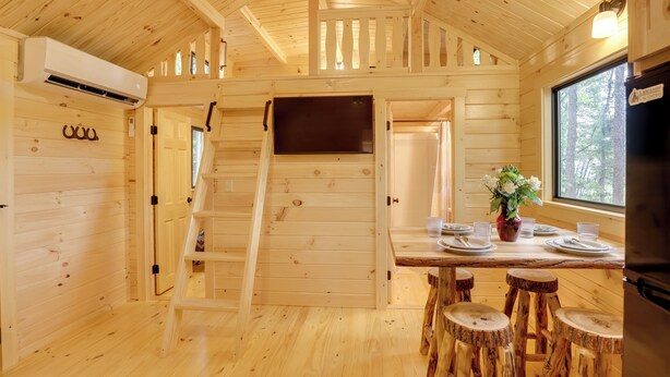 L’intérieur d’une cabane en bois comprend un coin repas, un escalier et une grande fenêtre.