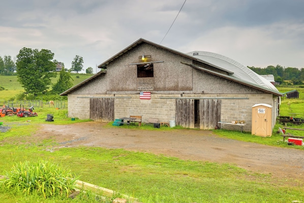 A barn with a single open door, a small table with chairs, and a flag. - Stunning Views! 3-cabin Retreat on 400-acre Farm (Middlebury Center)
