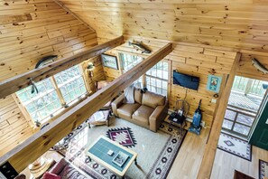 A wooden cabin interior with a loft area, a sofa, a coffee table, and a fireplace.