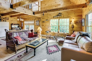A log cabin interior with a dining area, a sofa, a coffee table, and a fireplace. - Hike, Explore & Unwind: Rustic Maine Getaway (Machias)
