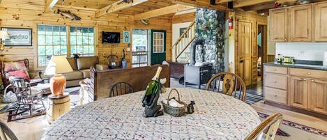 L’intérieur d’un chalet en bois comprend une table à manger, des chaises, une cheminée et un coin cuisine.