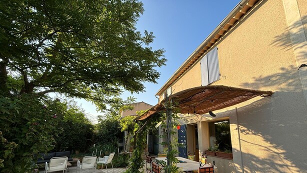 Een terras met buitenmeubilair, een pergola en een gebouw met een beige gevel.