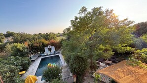 Een zwembad omringd door groen, een pergola en een overdekt zitgedeelte.