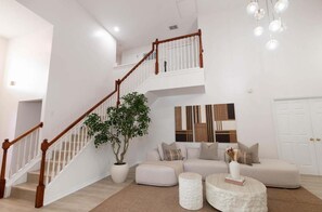 A spacious living area with a staircase, a large potted plant, a sectional sofa, and a coffee table. - Golf Course Retreat w/ Pool, Spa & Game Room, Disney (Davenport)