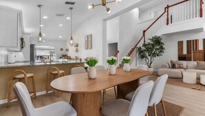 A spacious living area with a wooden dining table, grey chairs, and a staircase leading to an upper level. - Disney Villa: Pool, Spa & Mario Bros Game Room (Davenport)