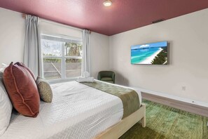 A bedroom with a bed, a window with curtains, a green chair, a wall-mounted TV, and a green carpet. - Golf Course Retreat w/ Pool, Spa & Game Room, Disney (Davenport)