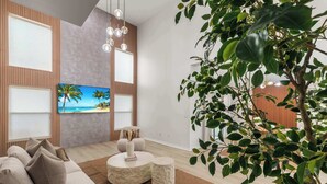 A modern living room with a large flat-screen TV, a sofa, a coffee table, and a potted plant. - Disney Villa: Pool, Spa & Mario Bros Game Room (Davenport)