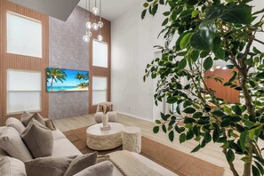A modern living room with a large flat-screen TV, a sofa, a coffee table, and a potted plant. - Golf Course Retreat w/ Pool, Spa & Game Room, Disney (Davenport)