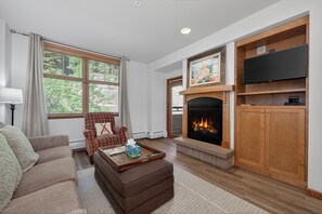 A living room with a fireplace, a television, a sofa, and a chair. - Zephyr Mountain Lodge Unit 1407 Private deck ski-in/ski-out on site amenities (Winter Park)